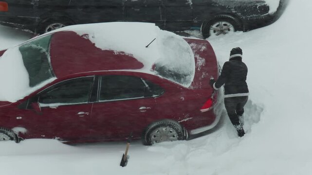 One person pushing red car stuck in deep snow, effort to free vehicle from winter snowdrift, challenging weather conditions, cold day