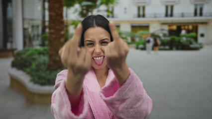 Fototapeta premium Hispanic woman in pink robe making a rude gesture with both middle fingers in an urban city street setting.