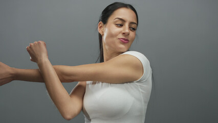 Obraz premium Young woman stretching against grey wall showcasing happiness and energy in an isolated studio environment with focus on fitness and personal well-being.