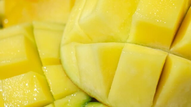 Juicy mango halves with cube cut pattern close-up rotation on yellow background