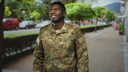 Soldier man smiling and looking up on a street in camouflage uniform and jacket, standing on a...