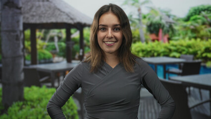 Fototapeta premium Woman smiling with hands on hips and visible face at resort poolside gazebo and outdoor patio; confidence optimism.