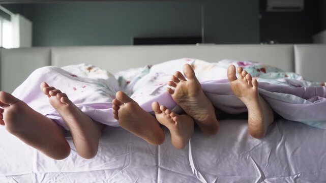 Family of Three Wiggling Feet Under Duvet in Bed