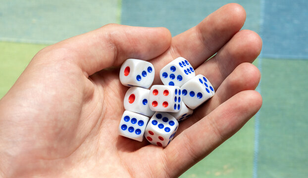 Hand holding eight white dice with red and blue pips, macro closeup of tabletop game cubes, random number generator, luck, probability and risk concept, gambling chance, statistics, decision making
