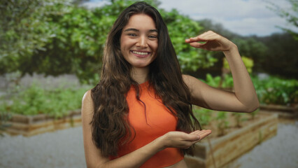 Naklejka premium Woman in an orange top frames empty space with hands among green foliage in a lush forest setting; joy.
