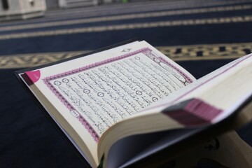 Holy Quran open on a prayer rug in a mosque - Islamic concept
 A high-quality close-up of the Holy Quran pages, placed on a traditional blue prayer rug inside a mosque. 