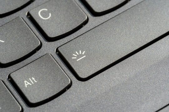 Laptop keyboard backlight toggle key closeup with illumination icon on spacebar, black matte plastic keys, computer shortcut hotkey button, technology control interface, macro detail, selective focus