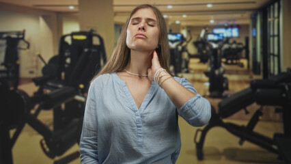 Fototapeta premium Woman touches her neck by a weight machine and treadmill amid gym equipment in a fitness building; relaxation.