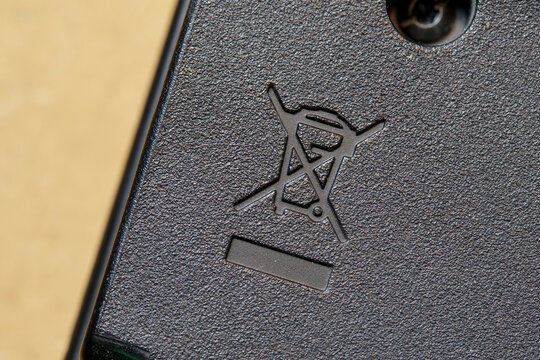 Crossed out wheeled bin symbol on electronic device casing, WEEE directive e-waste disposal icon, recycling and hazardous waste warning, textured black plastic macro closeup, no people