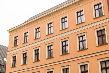 Obraz premium Orange European apartment building facade with rows of windows, classic tenement house architecture, urban residential rental property exterior, low angle view, symmetry, copy space sky, no people