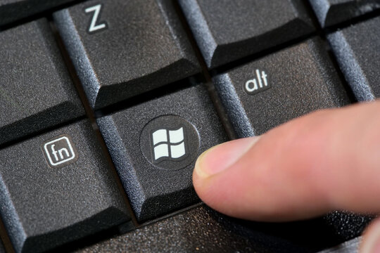 Finger pressing Microsoft Windows 7 logo key on computer keyboard, closeup macro of button, laptop key, obsolete operating system upgrade update concept, cybersecurity risk, end of support, one person