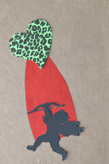 funky green paper heart with spots and black paper silhouette of a cherub with bow on red shape and brown background