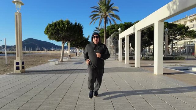 Hombre 50+ corriendo en el paseo mar&iacute;timo con dron en seguimiento frontal