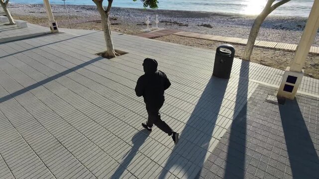 Hombre 50+ corriendo captado por dron alto y lateral en el paseo mar&iacute;timo