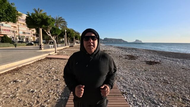 Hombre 50+ corriendo con seguimiento frontal con c&aacute;mara en el paseo mar&iacute;timo