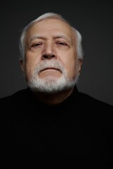 Obraz premium Elderly man with white beard looks directly at the camera in a simple light setting against a dark background