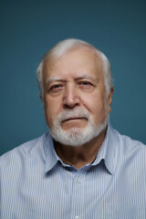 Fototapeta premium Elderly man with white beard wearing a blue striped shirt looking into the camera in a simple indoor setting