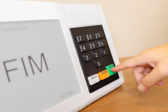 Urna eletr&ocirc;nica brasileira durante elei&ccedil;&otilde;es presidenciais, com eleitor pressionando o bot&atilde;o confirmar. Conceito de democracia, dever c&iacute;vico e processo eleitoral no Brasil.