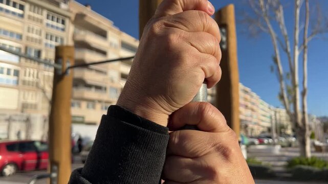 Plano detalle de manos de hombre 50+ apretando barra de ejercicio al aire libre