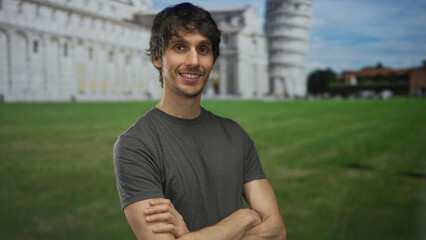 Young man smiling with crossed arms stands in front of leaning pisa tower building under bright daylight  quiet confidence. © Krakenimages.com