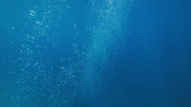 Slow-motion underwater footage moving through rising air bubbles in deep blue ocean water. Abstract marine scene with dynamic motion and natural light refraction.