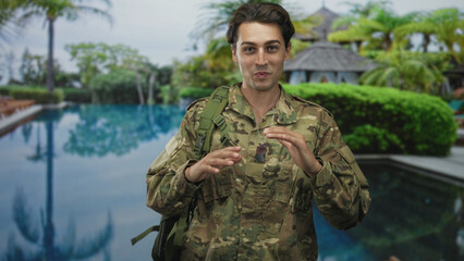 Man in camouflage uniform wearing dogtag frames his face with both hands beside a swimming pool...