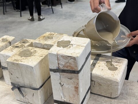 Demonstrates both casting and throwing techniques in the production of ceramic art . An artist pours liquid clay (slip) into plaster molds for ceramic pomegranate sculptures, wheel-turned clay pots.