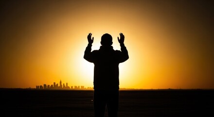 Fototapeta premium Man silhouette with raised arms toward bright sun over city skyline at horizon