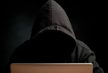 a hidden face hacker in a black hoodie sitting at a laptop