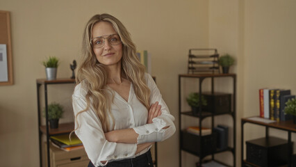 Woman in glasses standing confidently in an office environment with bookshelves and plants, exuding professionalism and confidence in her workplace setting. © Krakenimages.com