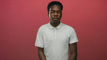 Young african american man wearing glasses stands with closed eyes in a red studio environment  serenity. © Krakenimages.com