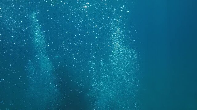 Slow-motion underwater footage moving through rising air bubbles in deep blue ocean water. Abstract marine scene with dynamic motion and natural light refraction.