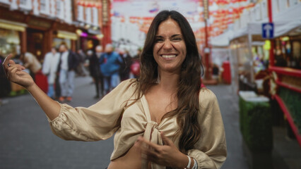 Fototapeta premium Woman in knotted blouse smiling with hand raised and mid dance on busy city street among market stalls and pedestrians; joy confidence.