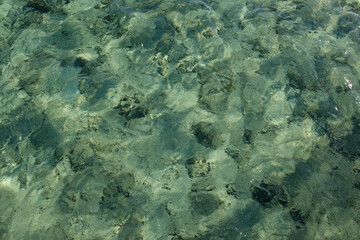 Fototapeta premium Clear turquoise water surface with visible rocks and sand beneath, creating a natural underwater scene in a tropical setting