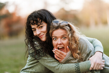 Fototapeta premium Two friends embrace joyfully in a sunlit park while enjoying a delightful afternoon filled with laughter and playful moments