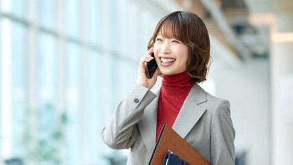 オフィスで電話対応をする日本人女性社員の明るいビジネスシーン,...