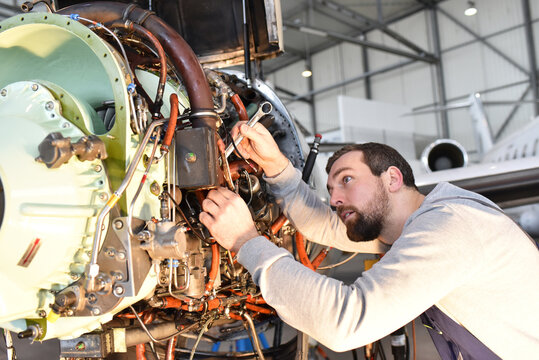 Aircraft mechanic repairs an aircraft engine in an airport hangar