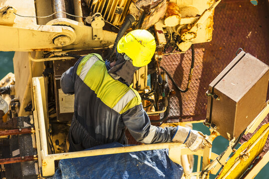 Overhead view of a seafarer wearing protective workwear and helmet conducting a visual inspection of a provision crane on the deck of a cargo ship.