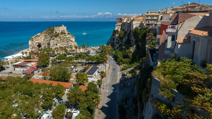 Aerial view of Tropea, Calabria, Italy. The Sanctuary of Santa Maria stands on its iconic rock formation, the historic town's buildings are perched high on the cliffs. A road leads toward the beach. © Stefano Tammaro
