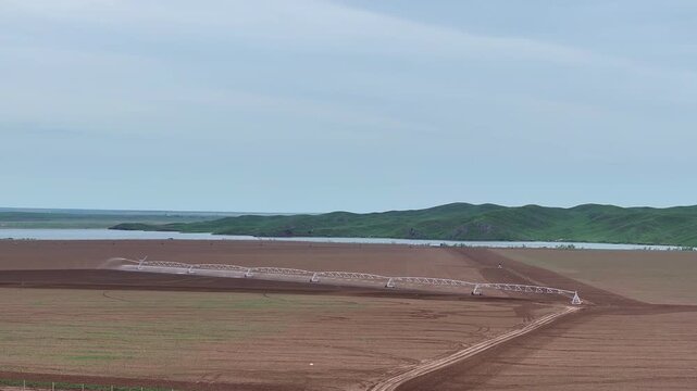 A wide cinematic view of a center-pivot irrigation system evenly watering agricultural land. The shot highlights the scale of the fields, the efficiency of modern agricultural technologies.