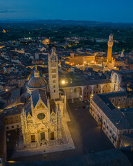 Obraz premium Aerial view of Siena Cathedral (Duomo di Siena) illuminated at blue hour, showcasing Gothic architecture and historic landmarks in the medieval city of Siena, Tuscany, Italy