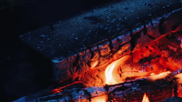 Cozy atmosphere with vibrant orange flames rising from burning wooden logs against a dark background, evoking warmth and comfort.