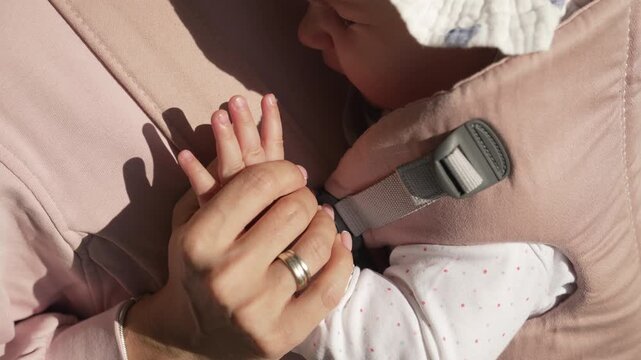 Mother and Baby Hands Holding in Ergonomic Carrier Outdoors, Close Up Detail