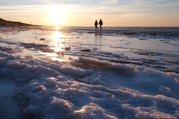 Naklejka premium Flooded forest with trunks of ancient trees (3000 years old) on the beach Lazy around Koszalin, Baltic Sea, West Pomeranian Voivodeship, Poland.Little silhouette of walking person on beach.