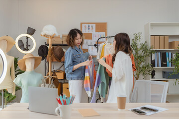 Two cheerful Asian women in a fashion studio happily taking a selfie while holding colorful...
