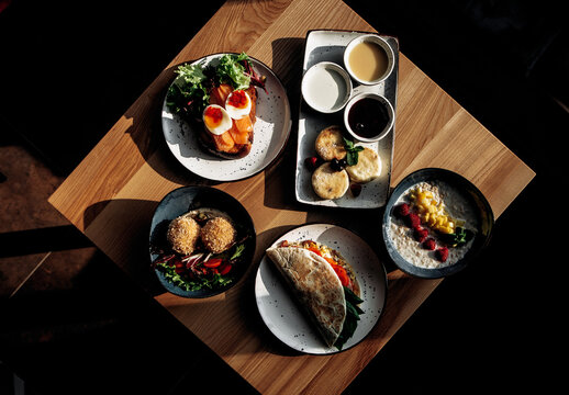 Overhead view of five different restaurant dishes arranged on a wooden table, showcasing a variety of gourmet meals. Perfect for menu or food photography.