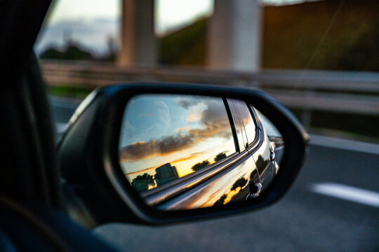 A car's rear view mirror shows a city skyline in the background