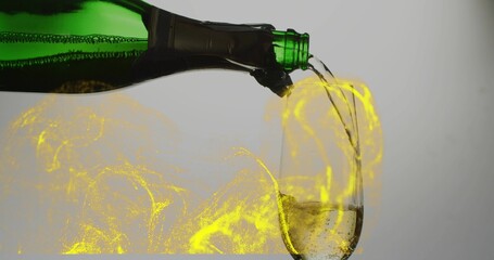 Tilting green bottle pouring fizzy liquid into champagne flute in studio yellow swirls, copy space
