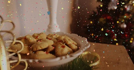 Showing white scalloped plate holding jam thumbprint cookies on wooden tabletop with holiday lights