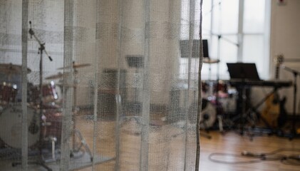 Medium shot capturing the installation of layered fabric curtains in a rehearsal room the folds and textures sharp while instruments in the room remain blurred.